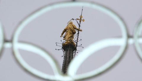 La estatua de la Virgen María en lo alto de la catedral gótica del Duomo se ve a través de los icónicos anillos de neón olímpicos antes de los próximos Juegos Olímpicos de Invierno de Milán-Cortina en Milán, Italia. (AP Photo/Luca Bruno)