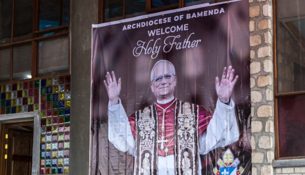 Le 12 avril 2026, à la cathédrale Saint-Joseph de Bamenda (dans le Nord-Ouest, région anglophone), une affiche souhaite la bienvenue au pape Léon XIV, sous les yeux d’un militaire armé. La venue du souverain pontife au Cameroun (15-18 avril) s’est déroulée dans un contexte marqué par des prêches très politiques pour et contre le président Biya et ses adversaires. Patrick Meinhardt/AFP