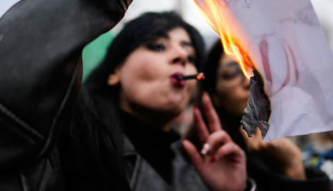 Una manifestante fuma un cigarrillo después de encenderlo en un cartel en llamas que representa al líder supremo iraní, el ayatolá Alí Jamenei, una imagen que se ha convertido en el símbolo de la revuelta actual, durante una concentración en apoyo a las manifestaciones antigubernamentales en Irán, en Yalova, Turquía, el 16 de enero de 2026. (AP Photo/Emrah Gurel)