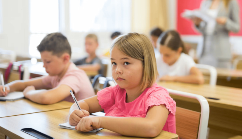 Varios niños escriben en clase, con una niña en primer plano. BearFotos/Shutterstock