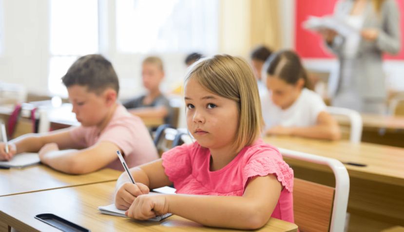 Varios niños escriben en clase, con una niña en primer plano. BearFotos/Shutterstock